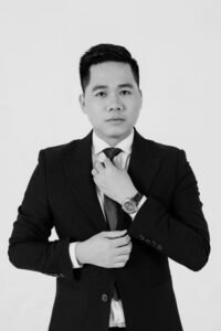 Black and white portrait of an Asian businessman in a suit adjusting his tie, exhibiting elegance and professionalism.