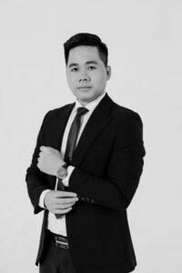 Confident Asian man in a suit posing in a studio setting, black and white photo.